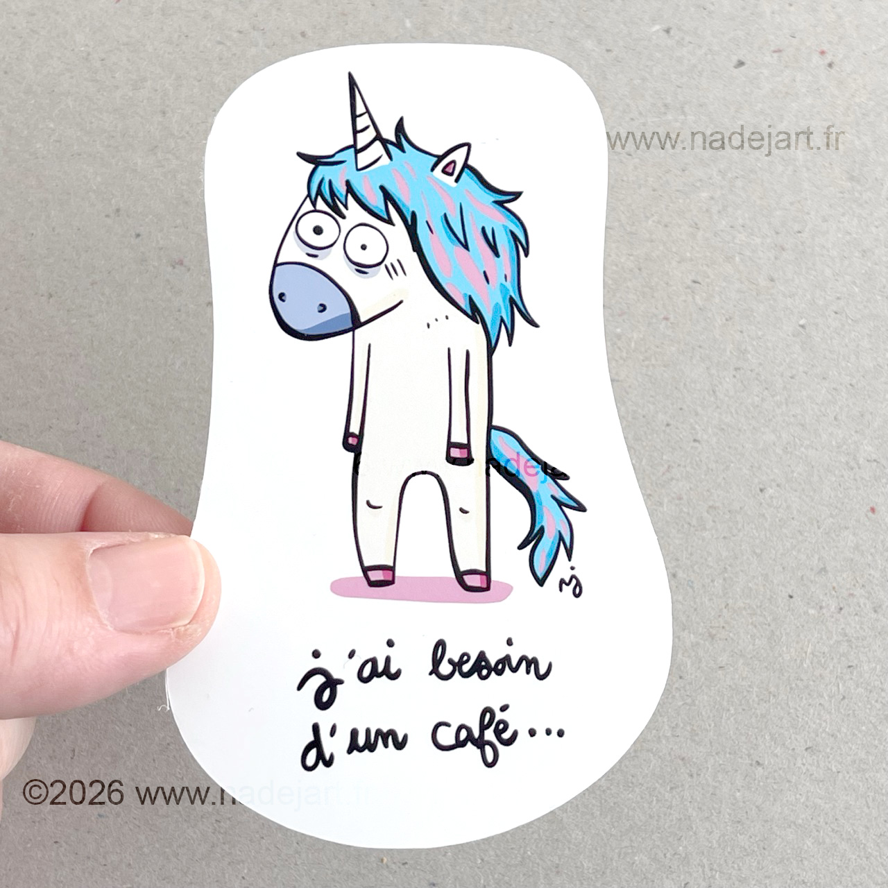 sticker en vynil blanc brillant avec une licorne avec une crinière bleue et une phrase d'humour sur le café ©2026 www.nadejart.fr