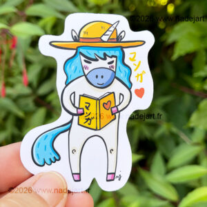grand sticker en vynil blanc avec une licorne avec une crinière bleue et qui lit un manga ©2026 www.nadejart.fr